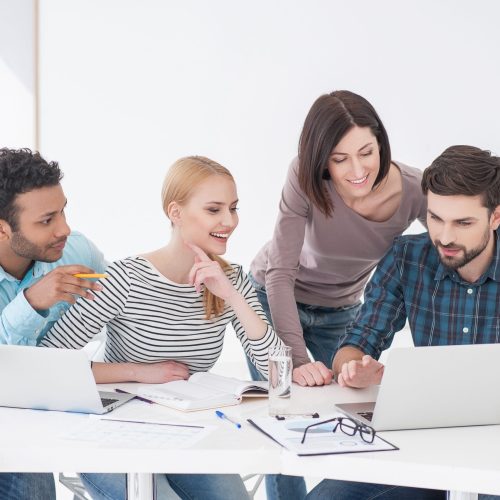 Injecting new ideas into group. Business people working on laptops around table at modern bright office indoors